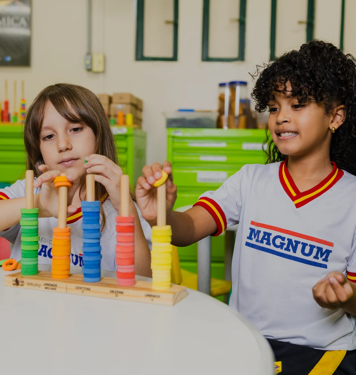 Duas crianças do Colégio Magnum brincando com um jogo de encaixe colorido sobre a mesa da sala de aula