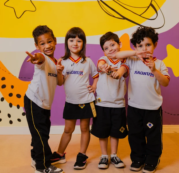 Quatro crianças do Colégio Magnum brincando juntas em frente a um painel colorido