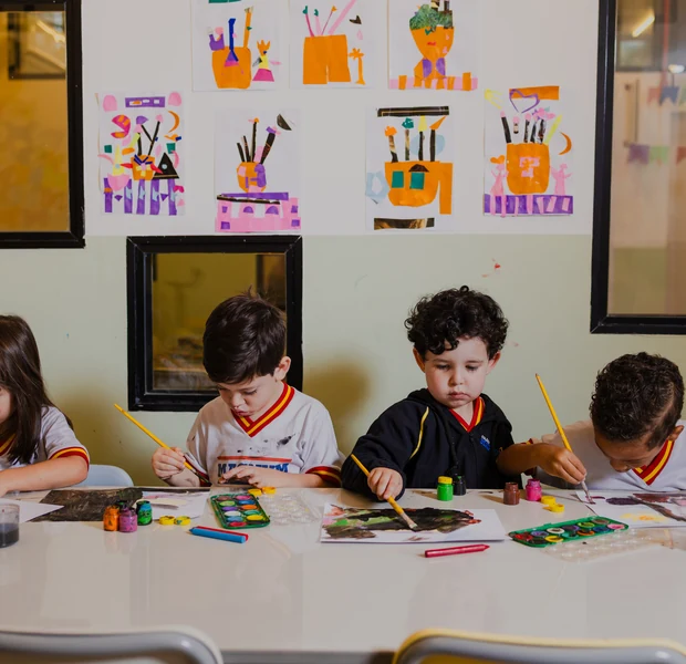 Crianças do Colégio Magnum em atividade na mesa da sala de aula, com trabalhos expostos na parede